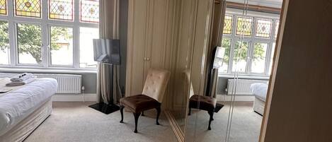 A bedroom with a large mirror, a bed, a chair, and a radiator.