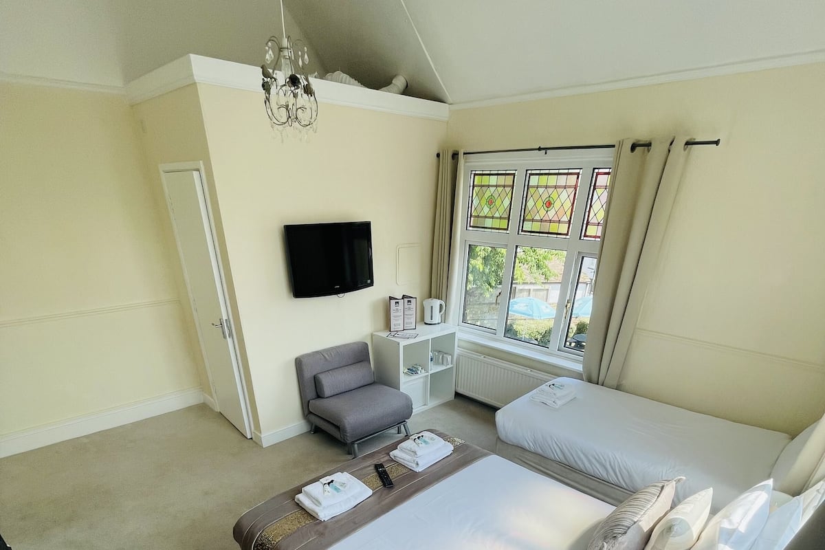 A hotel room with a bed, a chair, a TV, a window with curtains, and a radiator.
