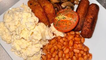 A plate of food including scrambled eggs, baked beans, mushrooms, sausages, and a slice of tomato.