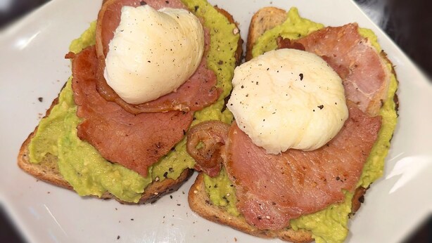 A plate with two open-faced sandwiches topped with avocado, ham, and poached eggs. - The Six Bells (Rochester)