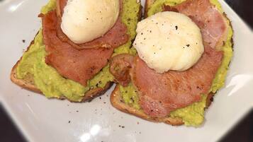 Un plato con dos sándwiches abiertos, cubiertos de aguacate, jamón y huevos pochados.