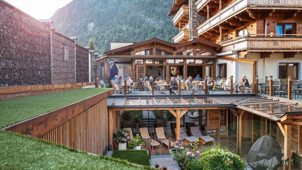 Una cabaña de madera con mobiliario exterior y una terraza con techo de cristal.