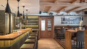 Zona de bar con mostradores de madera, varios taburetes y lámparas colgantes.