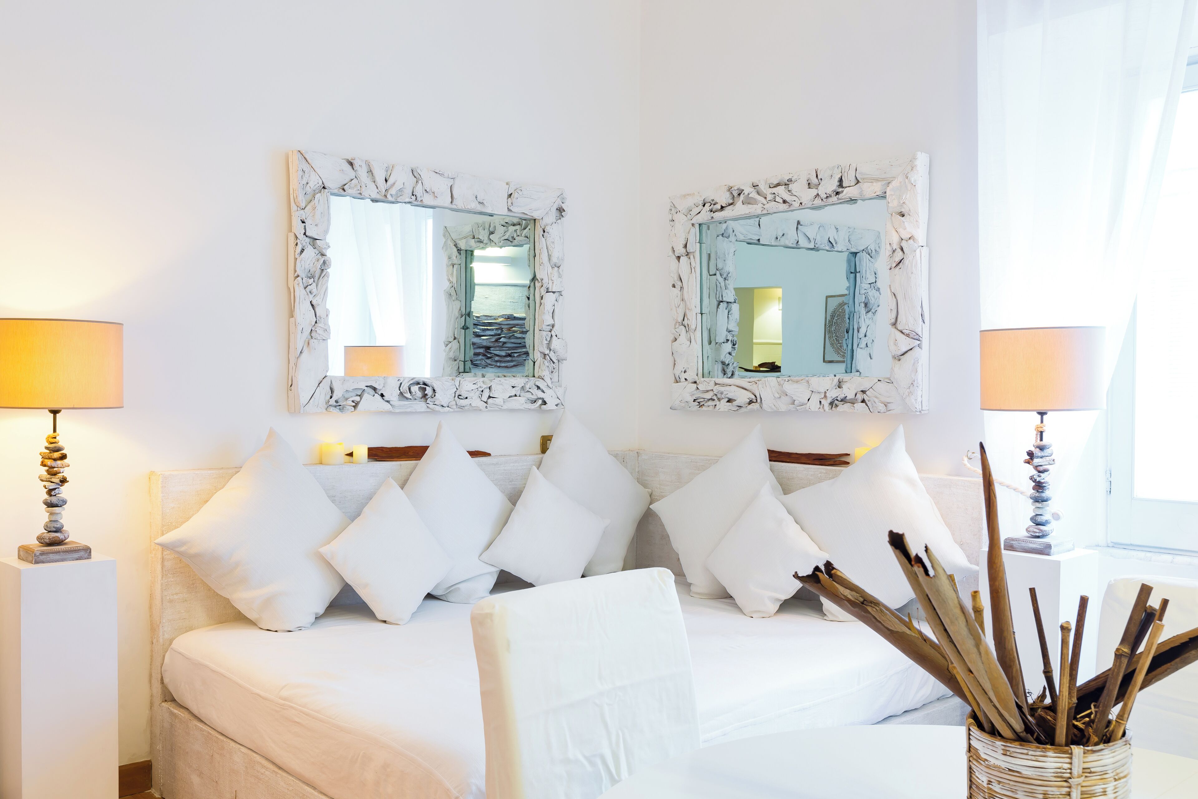 Une chambre d’hôtel avec un lit, deux lampes de chevet, un miroir et un vase contenant des branches.