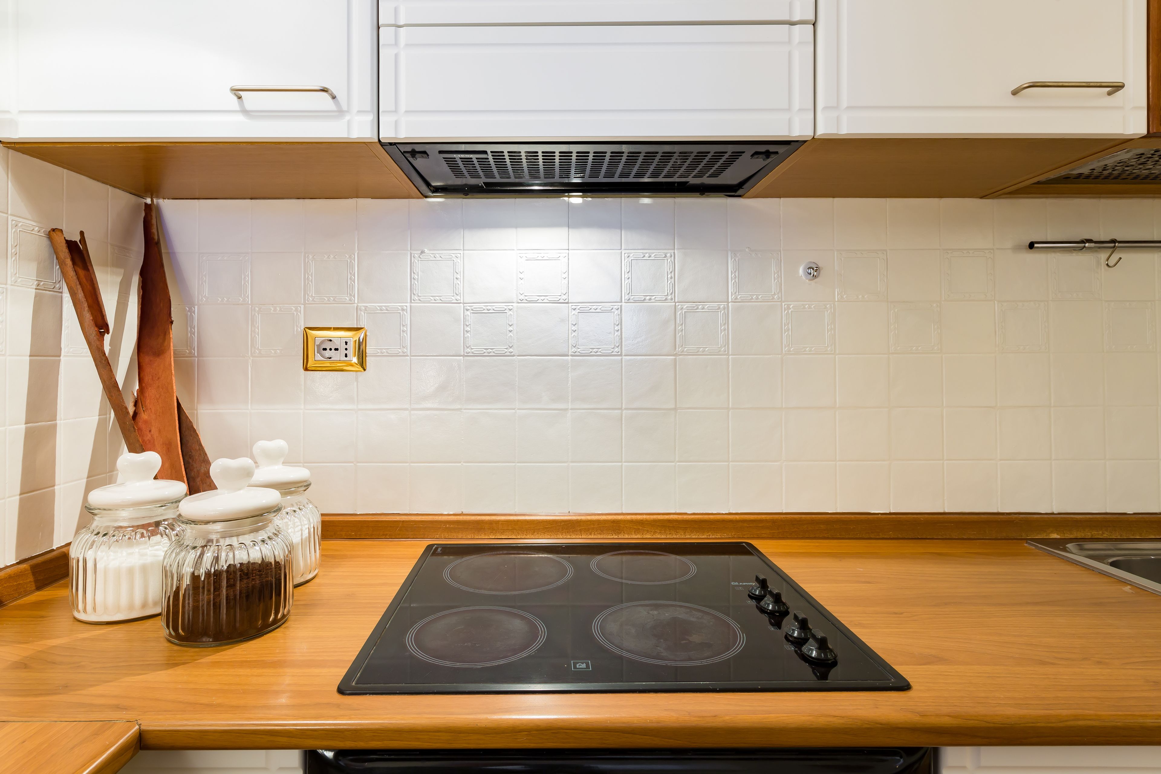 A kitchen with a black stovetop, white tiled backsplash, wooden countertop, and white cabinets.