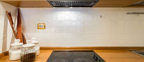 A kitchen with a black stovetop, white tiled backsplash, wooden countertop, and white cabinets.