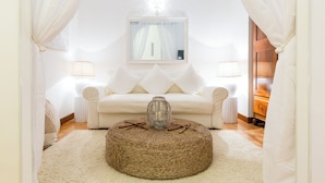 A cozy room with a white sofa, a round woven ottoman, and a mirror on the wall. - Casa Ripetta (Rome)