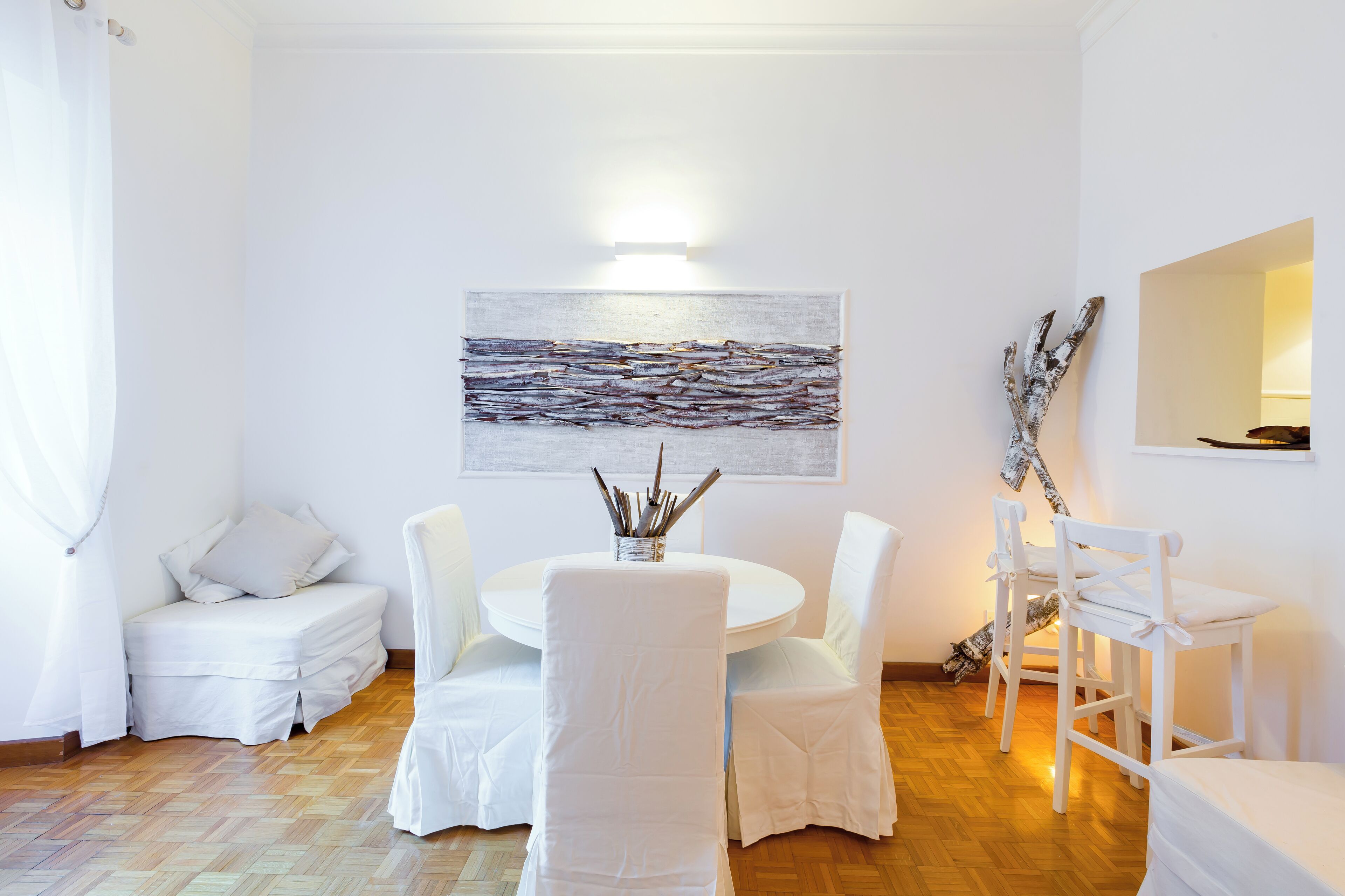 Een moderne, witte eetruimte met een ronde tafel, witte stoelen en een wanddecoratie.