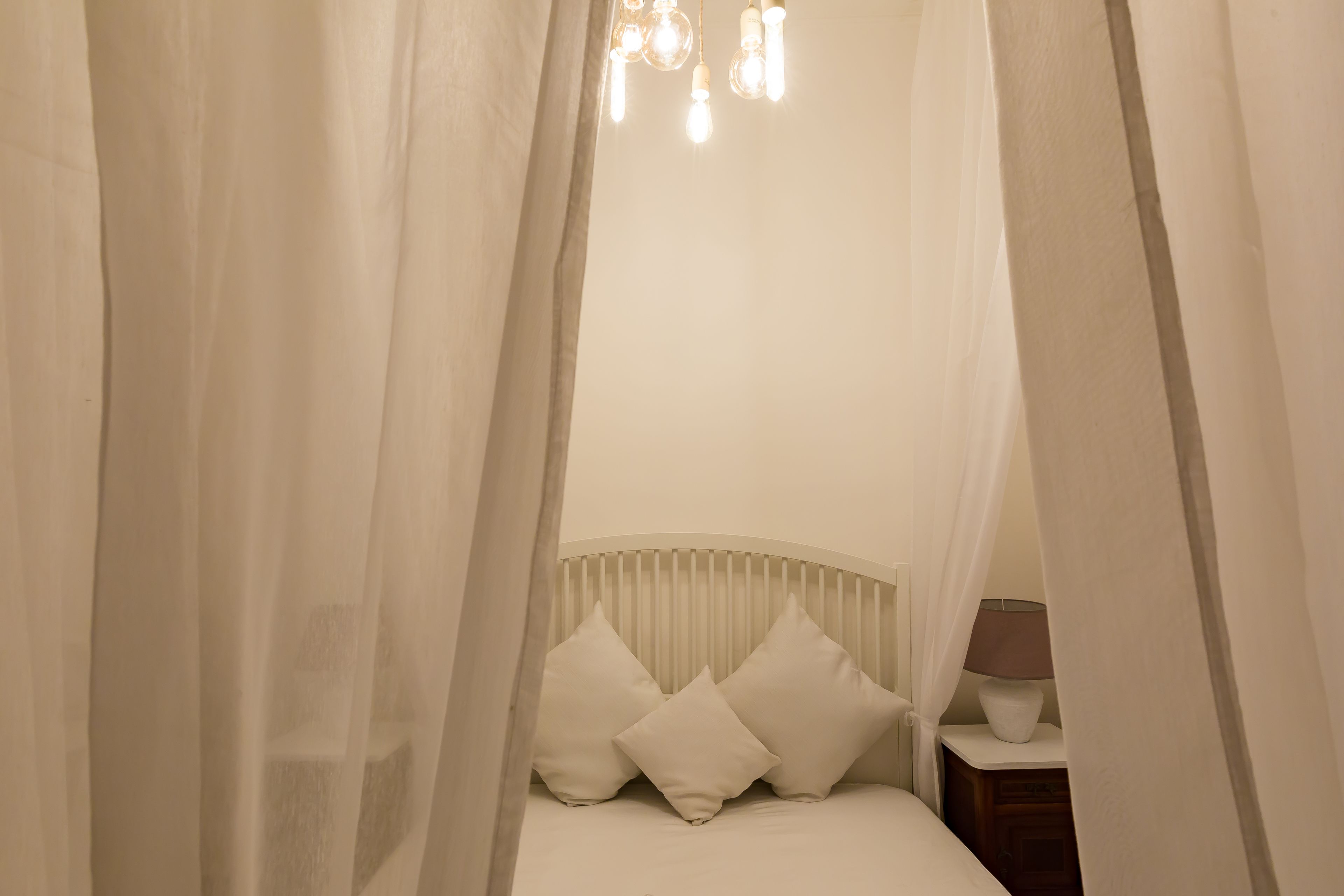 A bedroom with a canopy bed, white bedding, and a bedside table with a lamp.