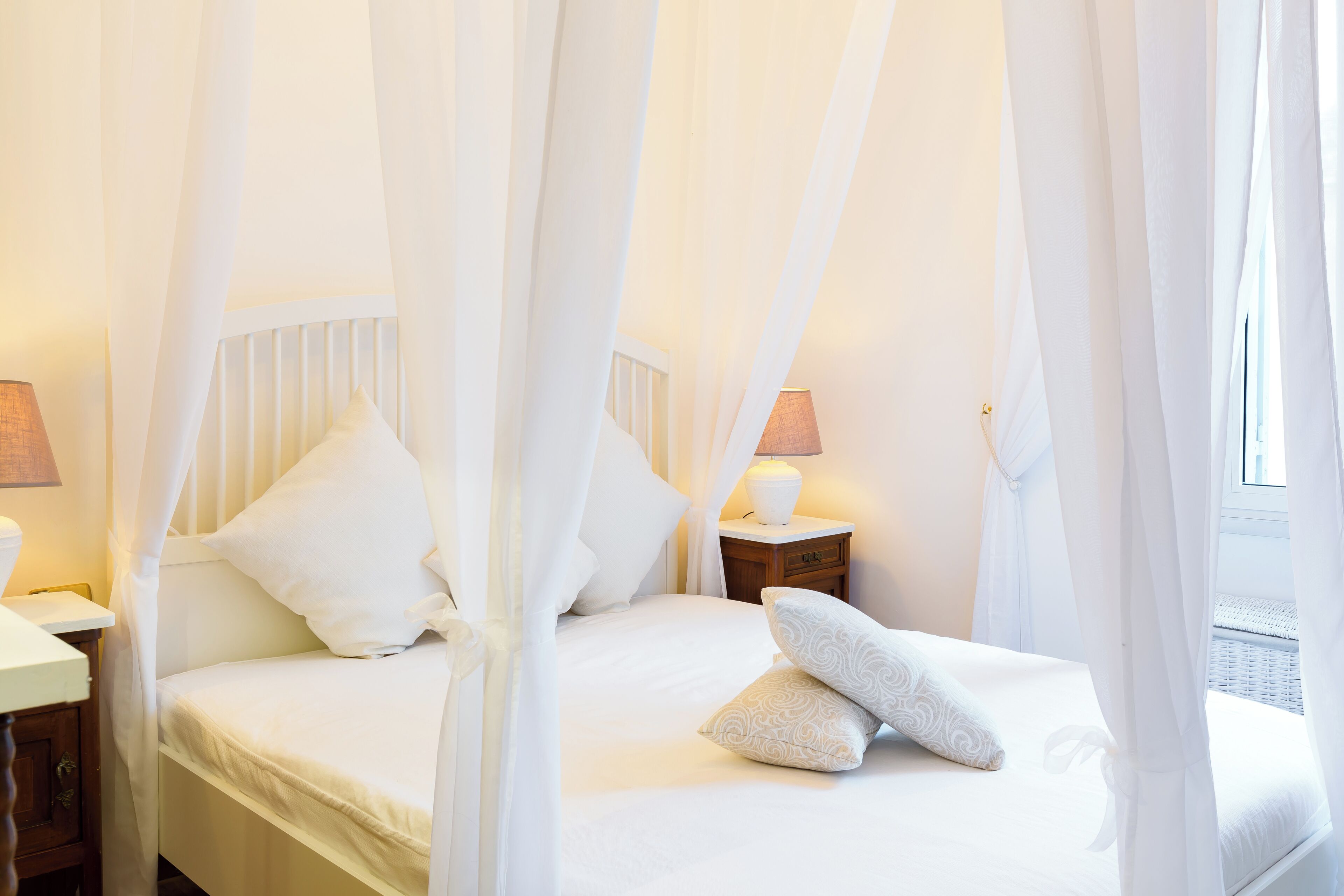 A bedroom with a canopy bed, white bedding, and bedside lamps.