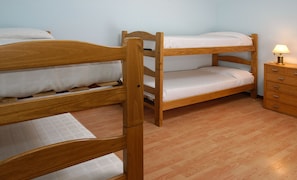 A bunk bed with a wooden frame and white bedding, a wooden dresser with drawers, and a lamp on the dresser. - Villa Campanario III (San Carlos de Bariloche)