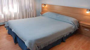 A bed with a wooden headboard, a blue blanket, and a wooden nightstand with a lamp.