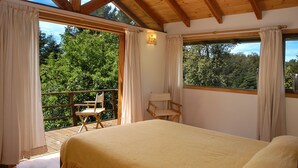 A bedroom with a large bed, a chair, and a balcony with a view of trees.
