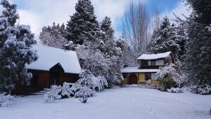 A snow-covered lodge with a wooden exterior, a covered porch, and a snow-covered driveway.