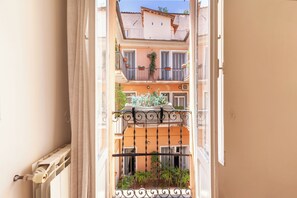 A view through an open window with a metal balcony railing, revealing a building with multiple balconies and potted plants. - Pantheon Luxury Gold Apartment (Rome)