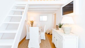 Un interior en tonos blancos con una escalera, un comedor con mesa y sillas, y un aparador con lámpara.