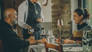 A restaurant setting with a table set for two, a waiter pouring wine, and a wine glass on the table.