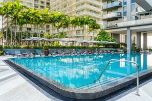A swimming pool with lounge chairs and umbrellas, surrounded by palm trees and a multi-story building. - Hyde Suites Midtown Miami (Miami)