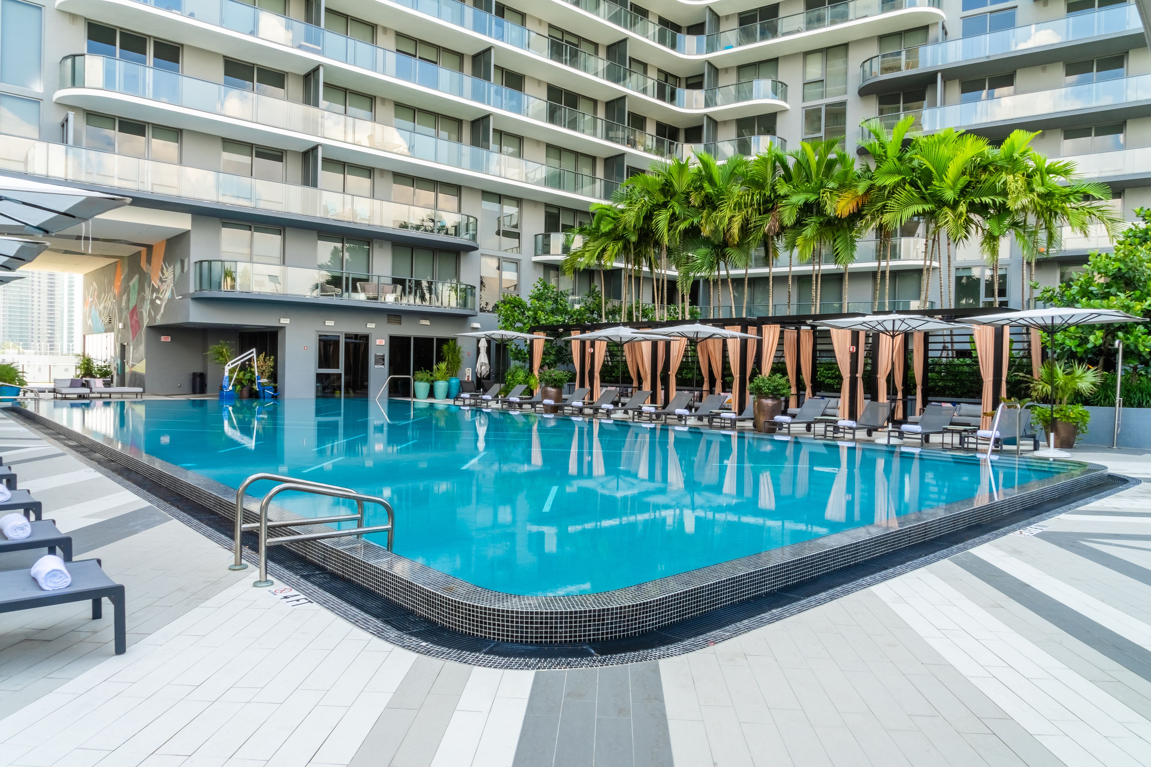 Un hotel moderno con piscina sul tetto, lettini prendisole e palme.