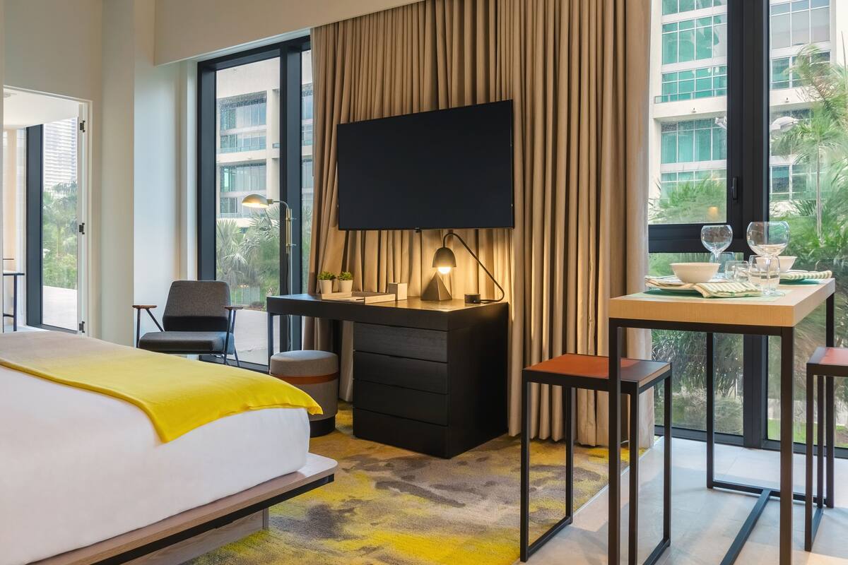 A modern hotel room with a bed, a desk, a TV, and a balcony with a table and chairs.