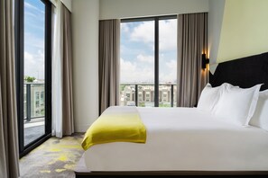 A hotel room with a large bed, a view of the city through a window, and a yellow throw blanket. - Hyde Suites Midtown Miami (Miami)