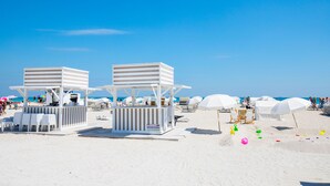 Ein Strand mit weißen Strandhütten, Sonnenschirmen und Liegestühlen.
