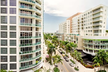 Two stationary bikes with digital displays, positioned in front of large windows overlooking a cityscape with high-rise buildings and palm trees. at Hyde Suites Midtown Miami