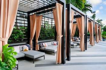 A swimming pool with lounge chairs and umbrellas, surrounded by palm trees and a modern building. at Hyde Suites Midtown Miami