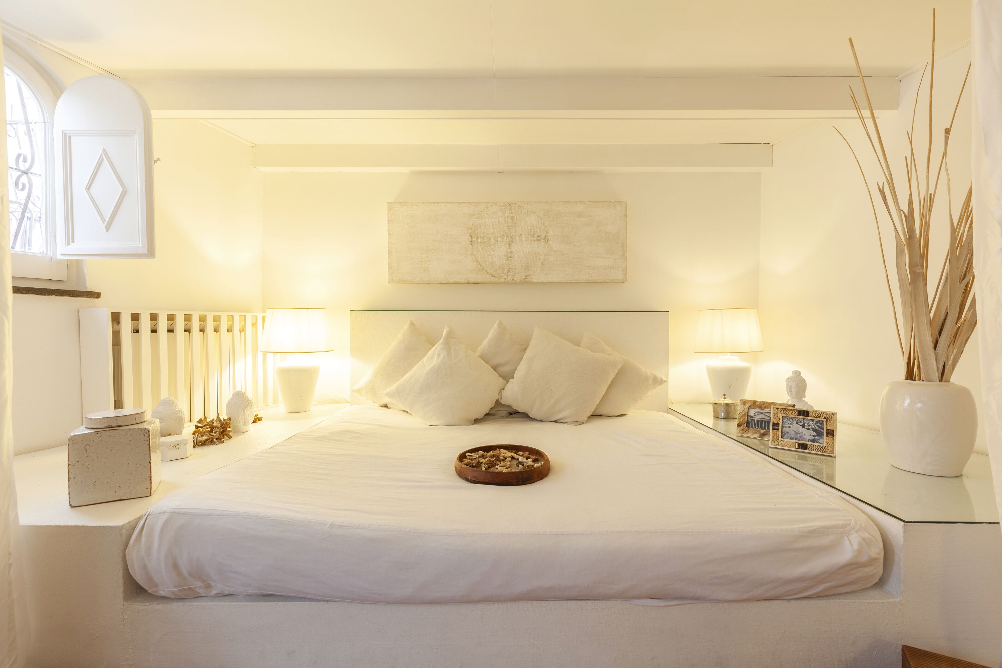 Un dormitorio minimalista con una cama grande, lámparas de noche, una mesita de noche con un florero y un radiador.