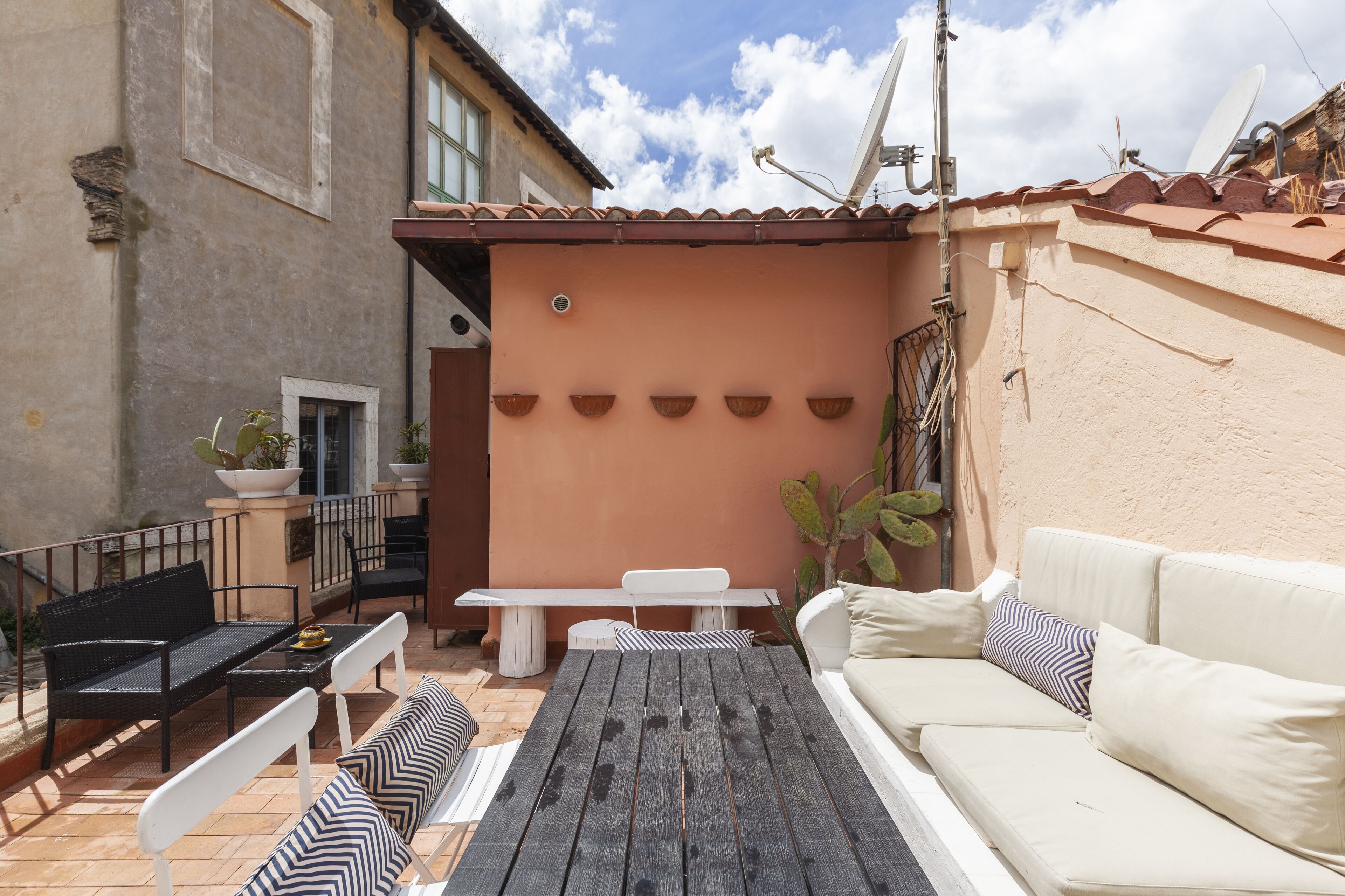A patio with a white sofa, black and white striped bench, and a wooden table.