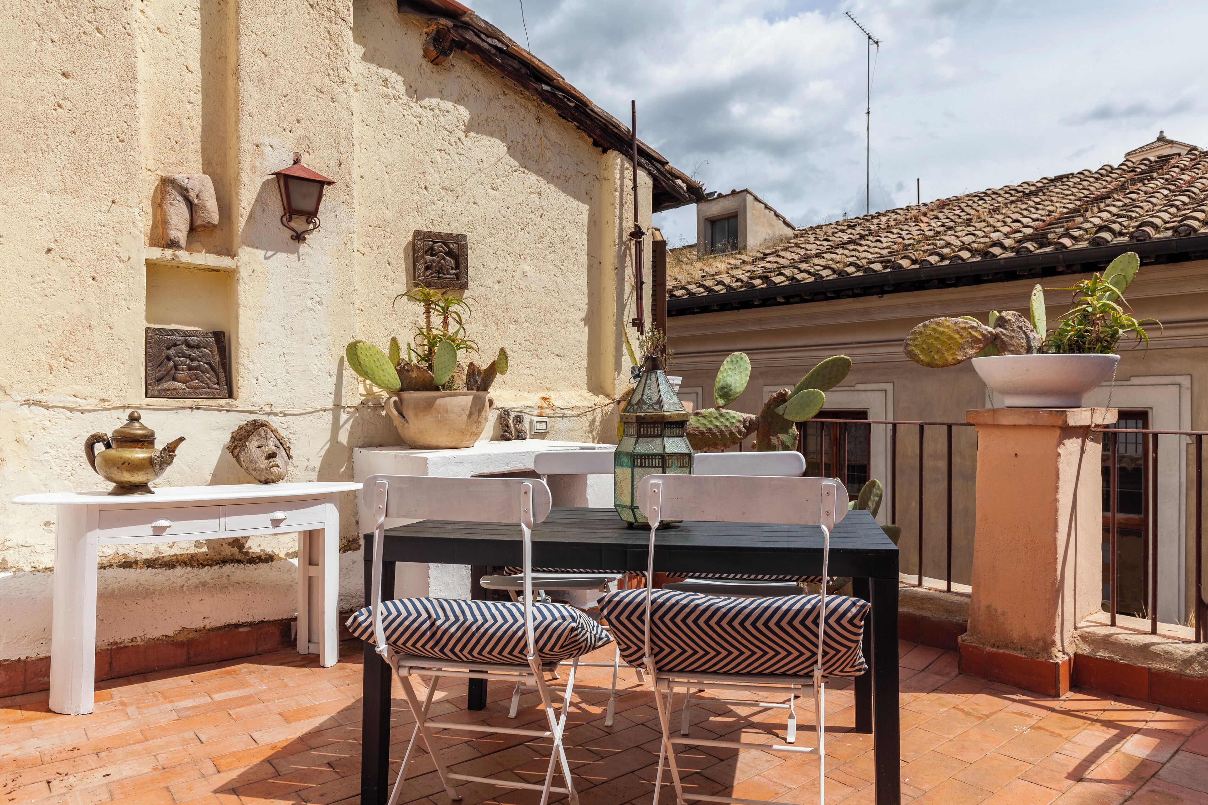 An outdoor patio with a table and chairs, potted plants, and a wall with decorative elements.