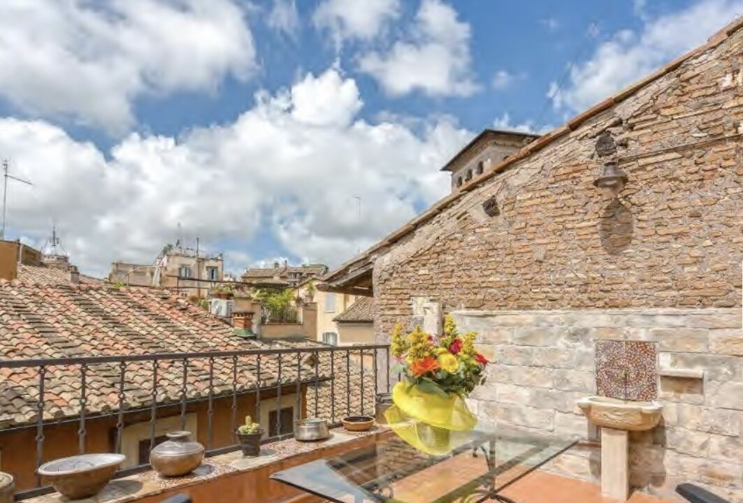 A rooftop terrace with a stone wall, a metal railing, and a flower arrangement.