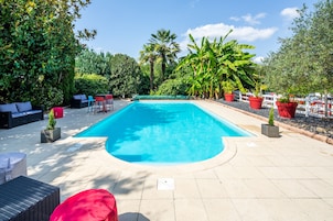 Piscina retangular com deck revestido, rodeada por plantas em vasos e móveis de exterior.