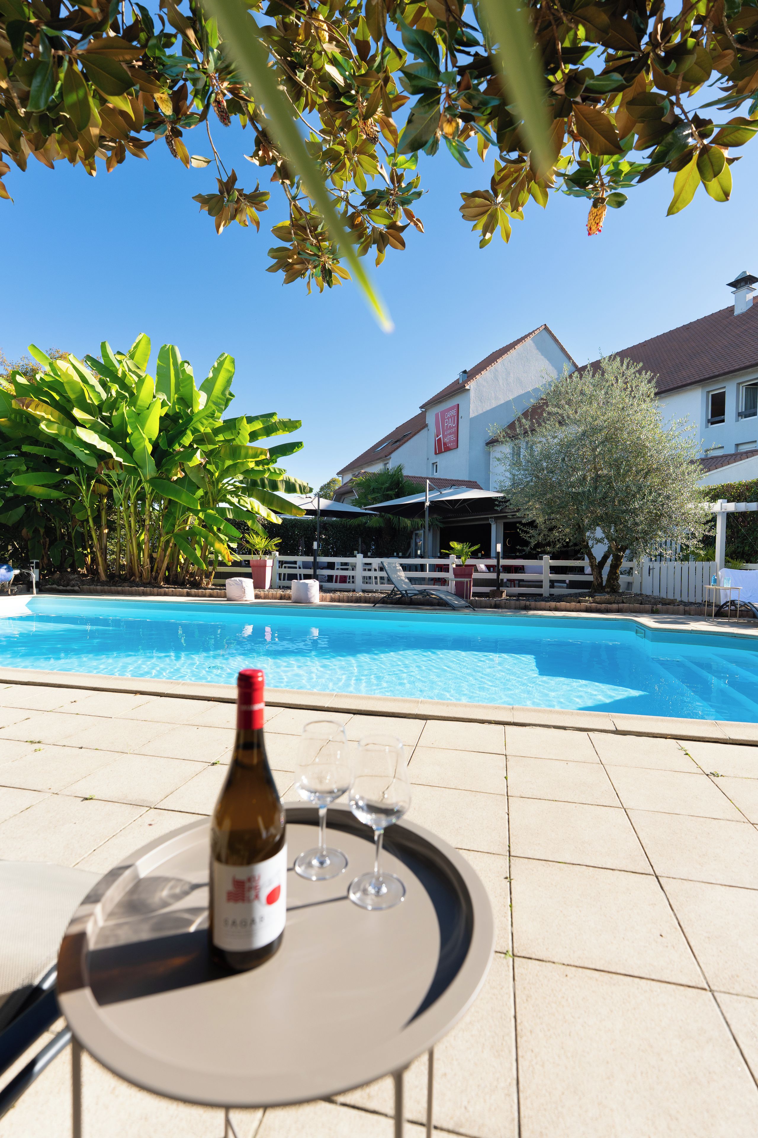 A poolside setting with a table, a bottle of wine, and glasses.