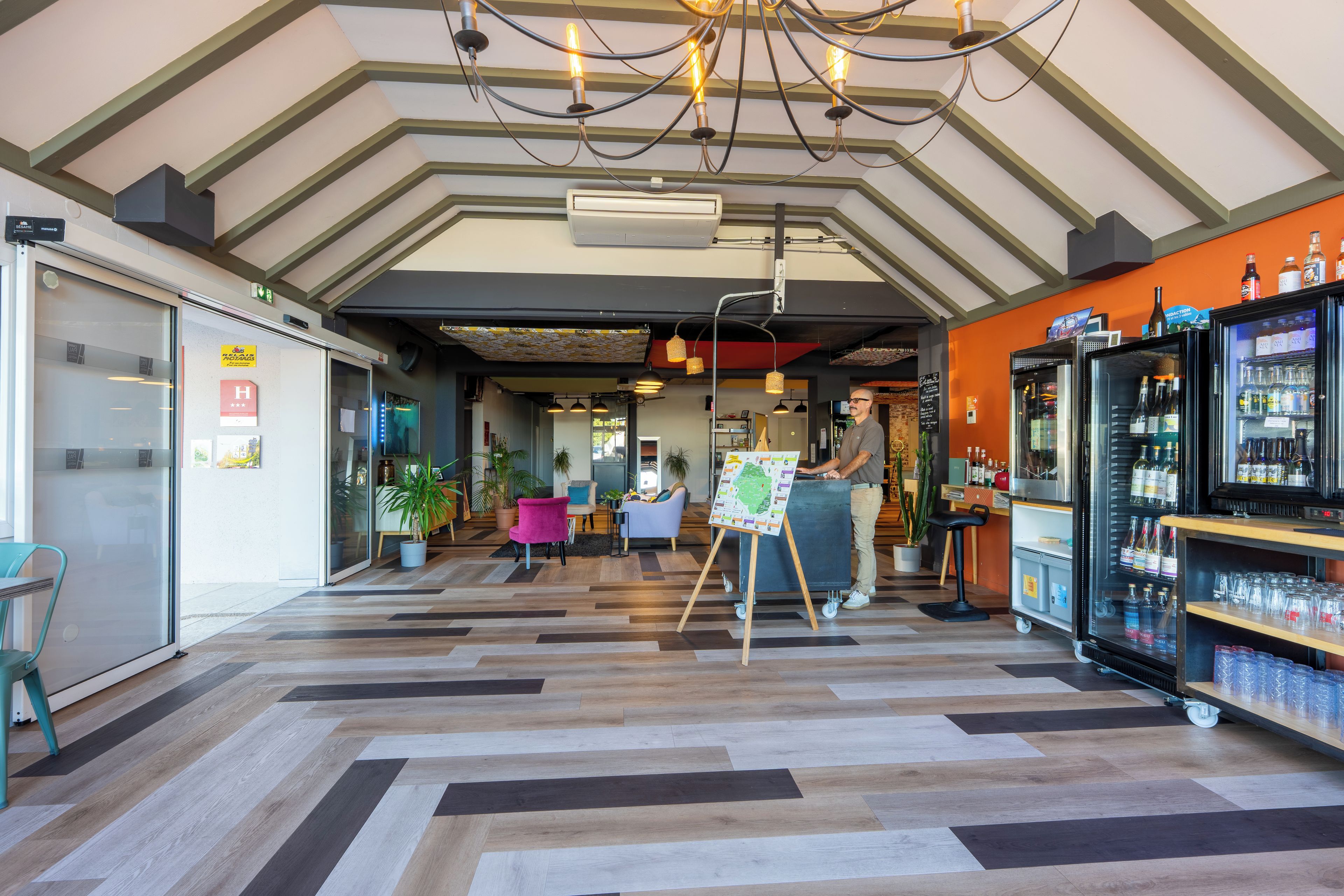 A modern interior with a herringbone floor pattern, a bar area with a bartender, and a refrigerator stocked with beverages.