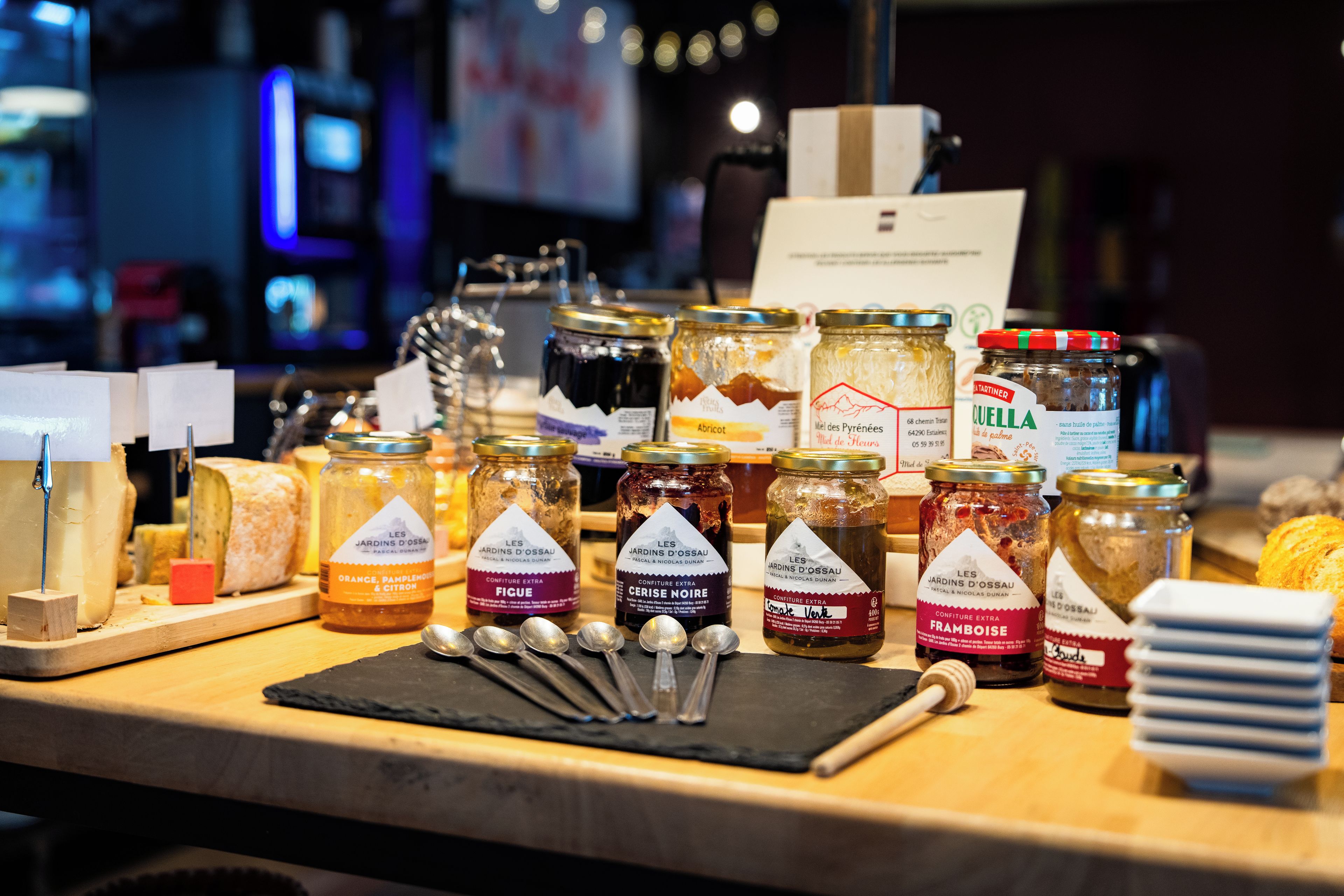 A variety of food items, including jars of preserves and cheese, on a wooden counter.