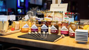A variety of food items, including jars of preserves and cheese, on a wooden counter.