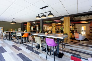 A modern cafe with multiple seating areas, including bar stools and chairs, and a variety of hanging pendant lights.