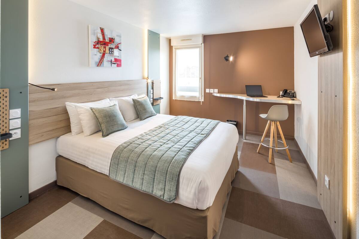 A modern hotel room with a large bed, a desk, and a TV mounted on the wall.