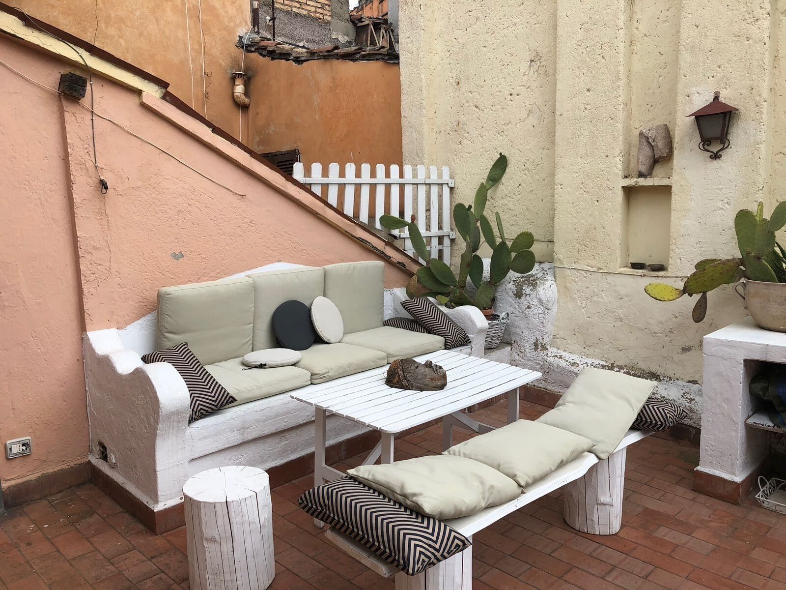 Un espace patio aménagé avec un canapé blanc, deux fauteuils blancs, une petite table et un cactus.