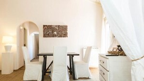 Une pièce avec une table et des chaises blanches, une lampe et une œuvre d’art abstraite accrochée au mur.