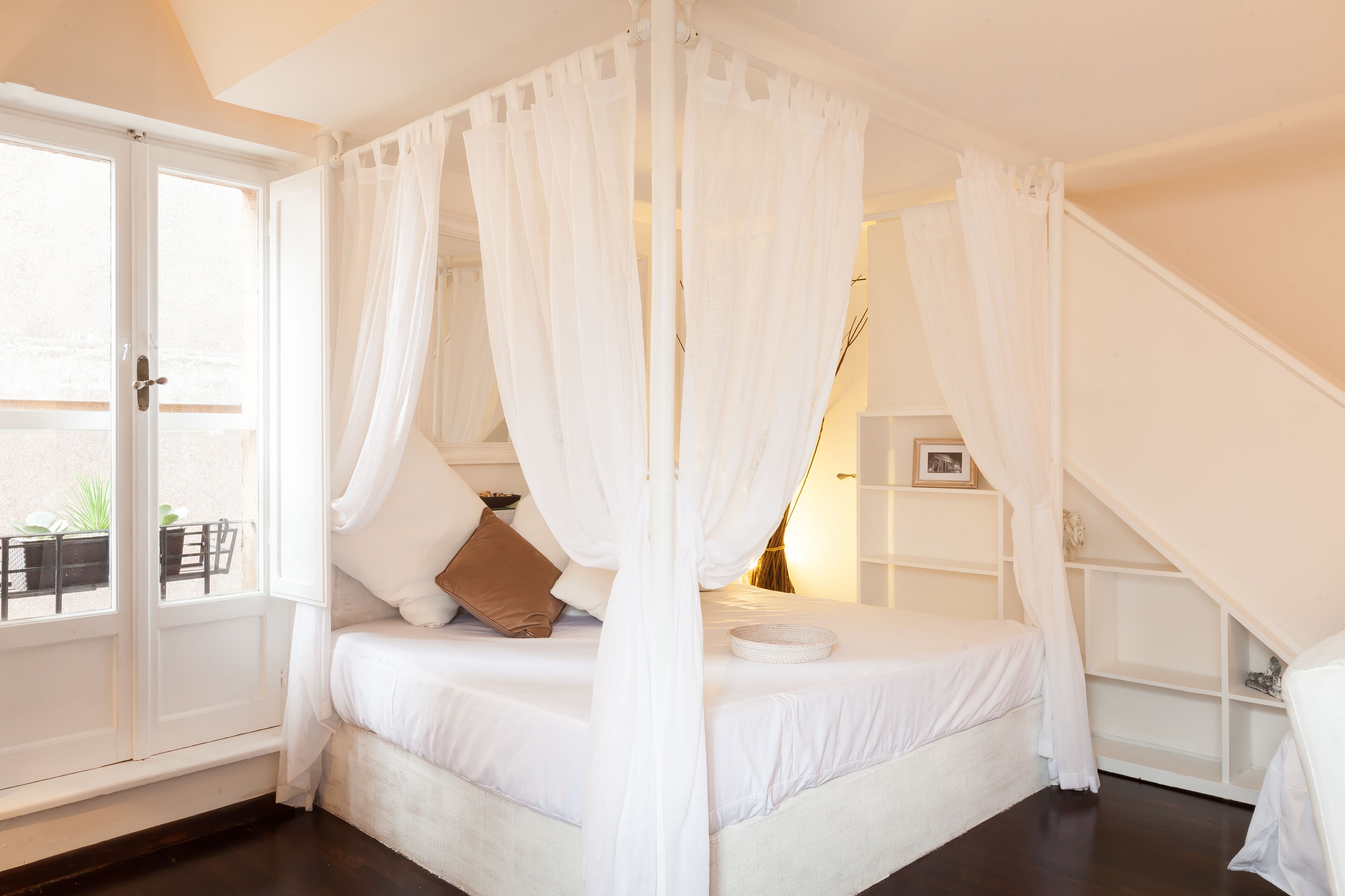A bedroom with a four-poster bed, white bedding, and a white canopy.