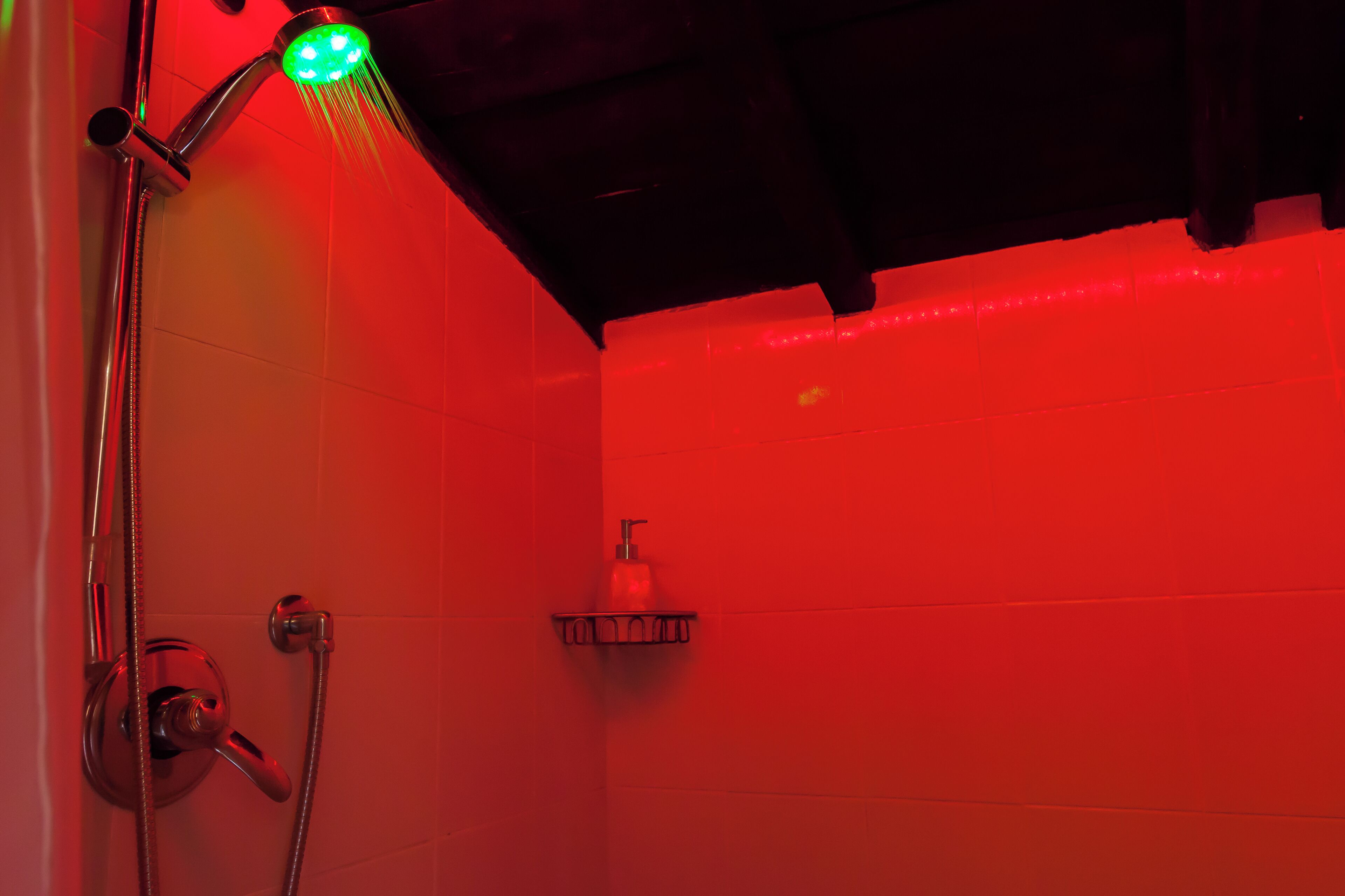 Une douche avec un éclairage vert, une douchette à main et un robinet mural.