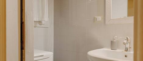 Une petite salle de bain propre, équipée de toilettes, d’un lavabo et d’un miroir.