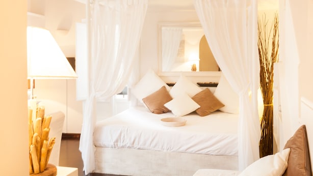 Un dormitorio con cama a dosel, ropa de cama blanca y una mesita de noche con lámpara y objetos decorativos.