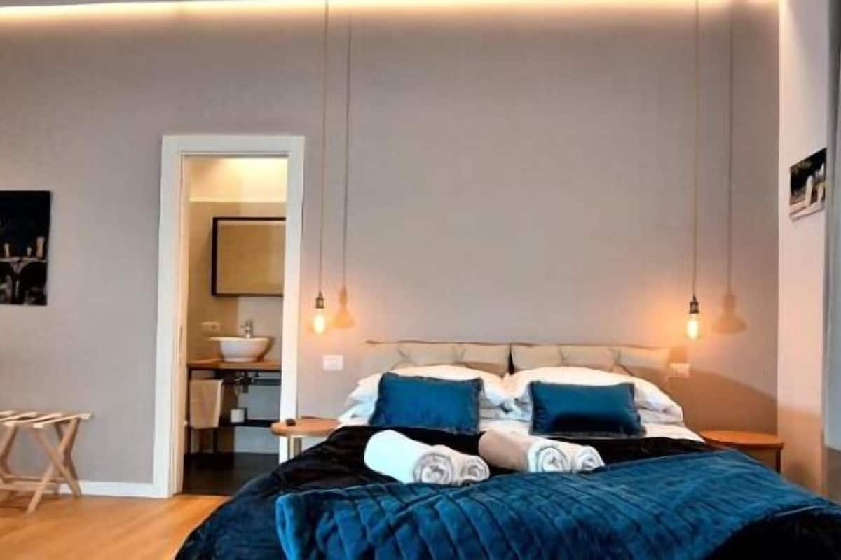 Una camera d'albergo moderna con un letto, comodini, una poltrona e un piccolo tavolino.