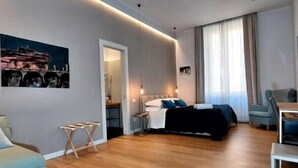 A modern hotel room with a bed, a desk, a chair, a small table, and a painting on the wall. - Vatican Rome Suite (Rome)