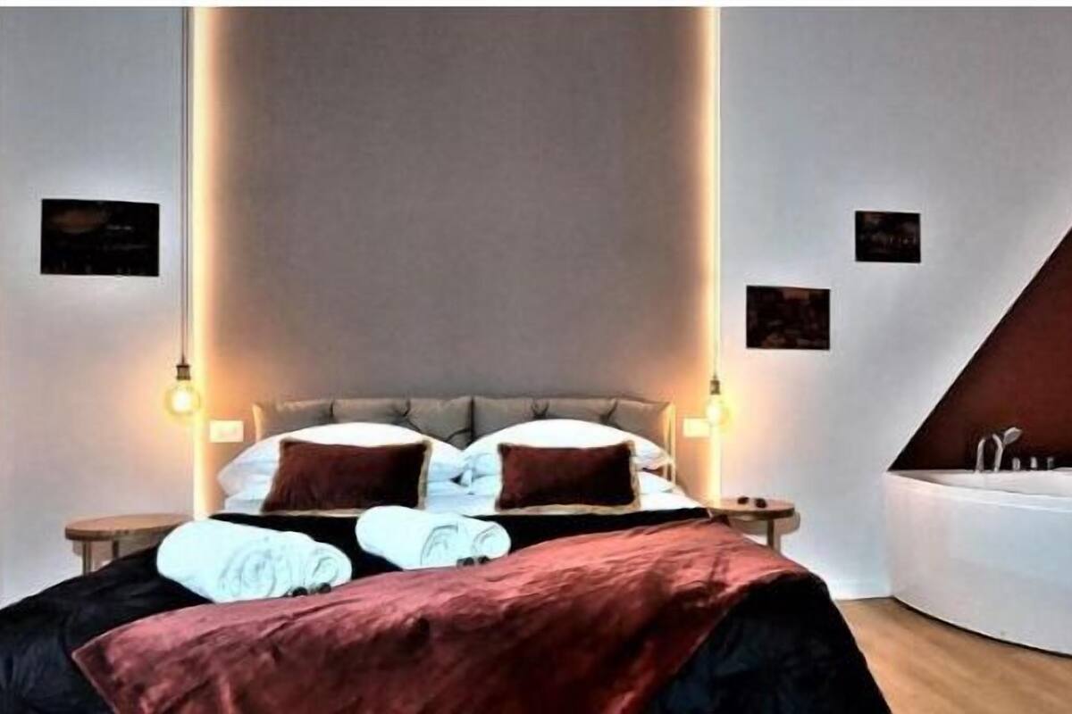 Una camera da letto moderna con un letto grande, una vasca idromassaggio a incasso e luci a parete.