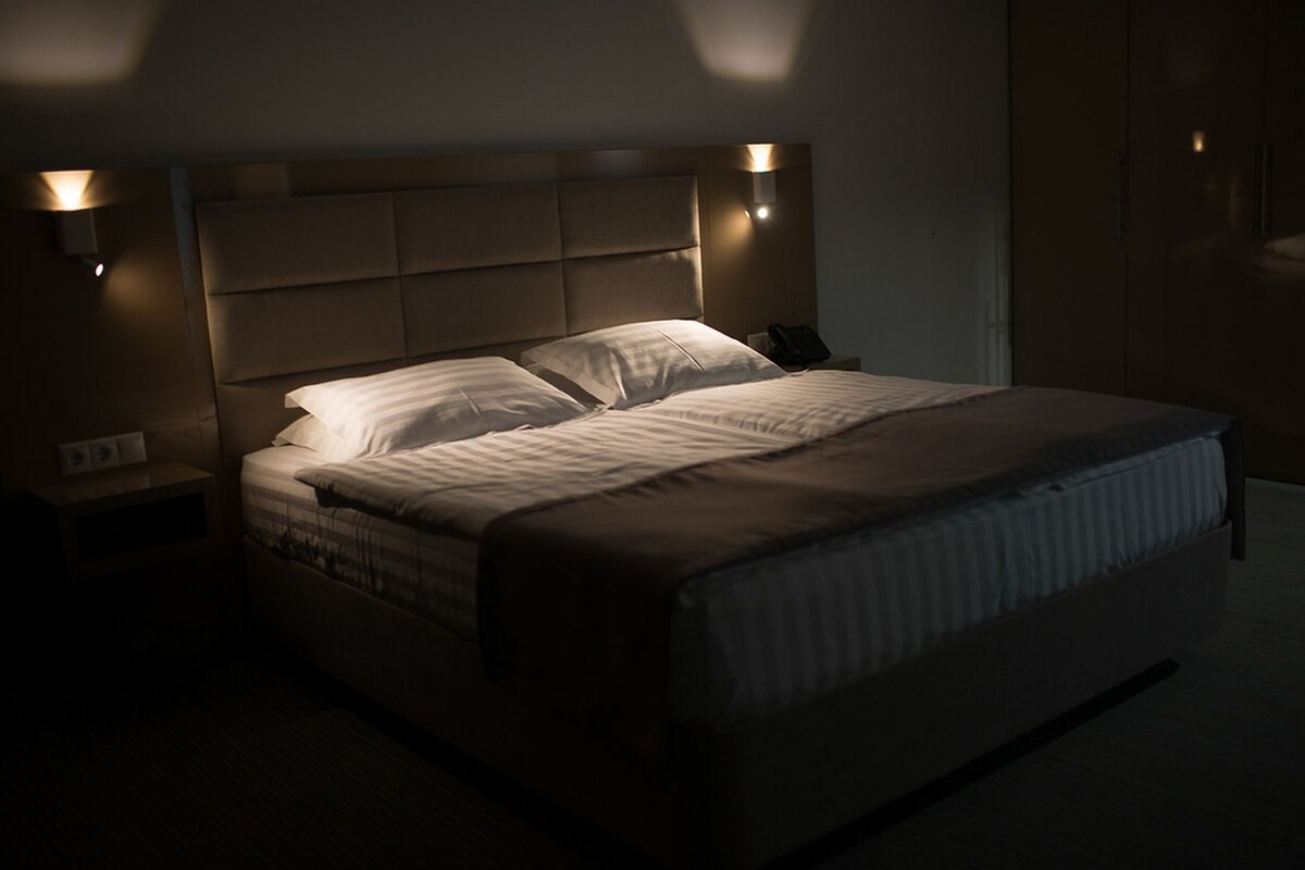 Un dormitorio moderno con una cama grande, un cabecero con iluminación integrada y una mesita de noche con un teléfono.