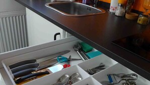 Eine Küche mit einer Spüle aus Edelstahl, einem Wasserkocher und verschiedenen Küchenutensilien auf der Arbeitsfläche.